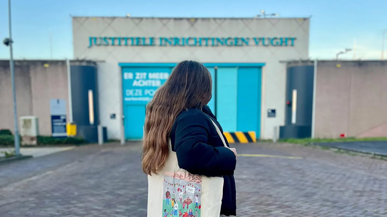 Vrouw met lange haren en tas staat voor de ingang van Justitiële Inrichtingen Vught.