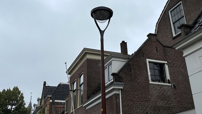 Straatlantaarn, gevels en dakken van huizen onder een bewolkte hemel.