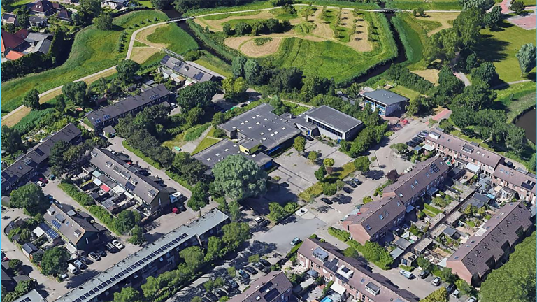 Luchtfoto van een woonwijk met groene parkachtige gebieden, zicht op rijtjeshuizen en parkeerplaatsen omgeven door bomen.