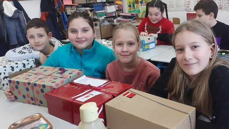 Kinderen in een klaslokaal zitten aan een tafel met cadeaus voor zich.